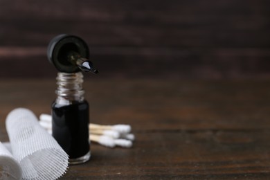 Photo of Bottle of iodine with dropper, cotton swabs and bandage on wooden table, closeup. Space for text