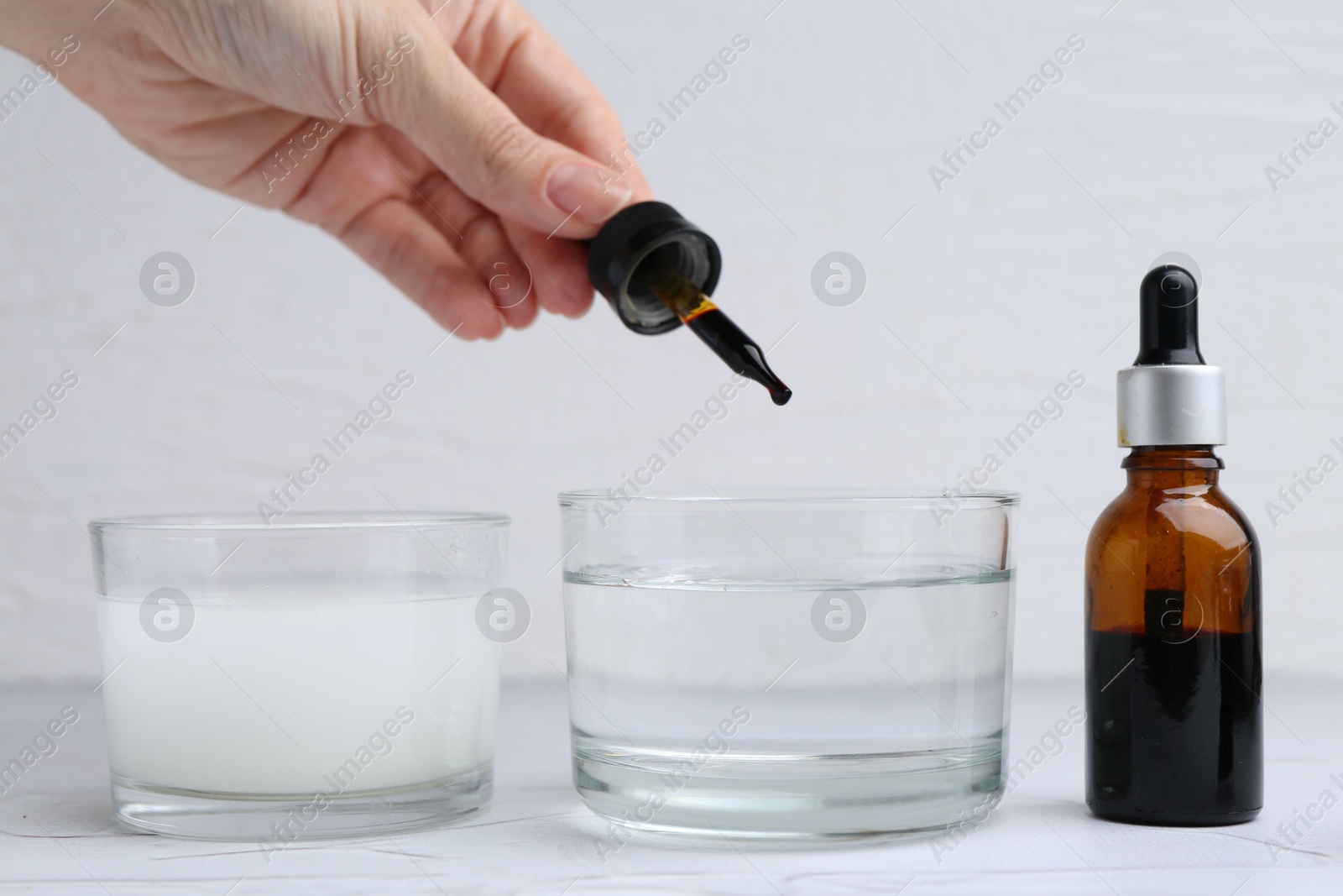 Photo of Iodine starch test. Woman dripping iodine into glass of water at white table, closeup