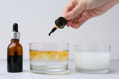 Photo of Iodine starch test. Woman dripping iodine into glass of water at white table, closeup