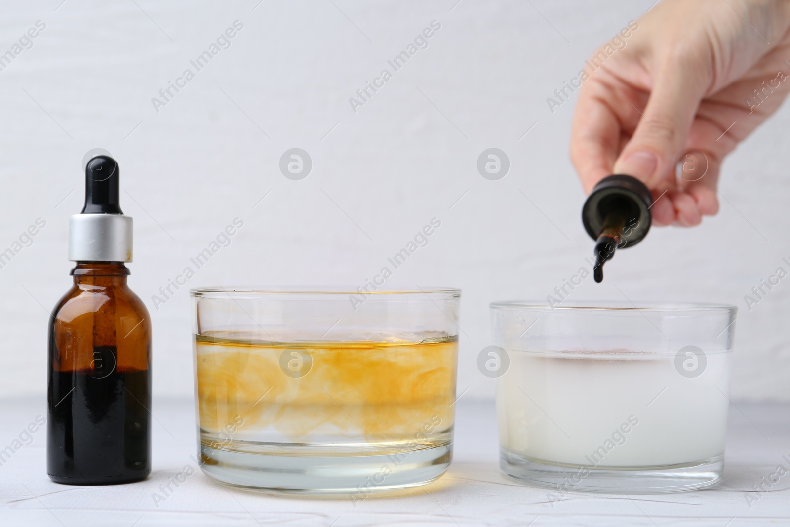 Photo of Iodine starch test. Woman dripping iodine into glass of water containing starch at white table, closeup