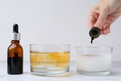 Photo of Iodine starch test. Woman dripping iodine into glass of water containing starch at white table, closeup