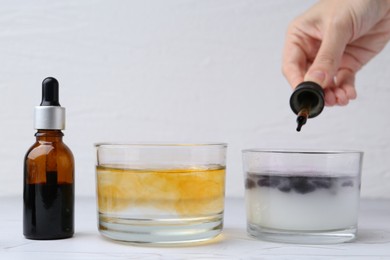 Photo of Iodine starch test. Woman dripping iodine into glass of water containing starch at white table, closeup