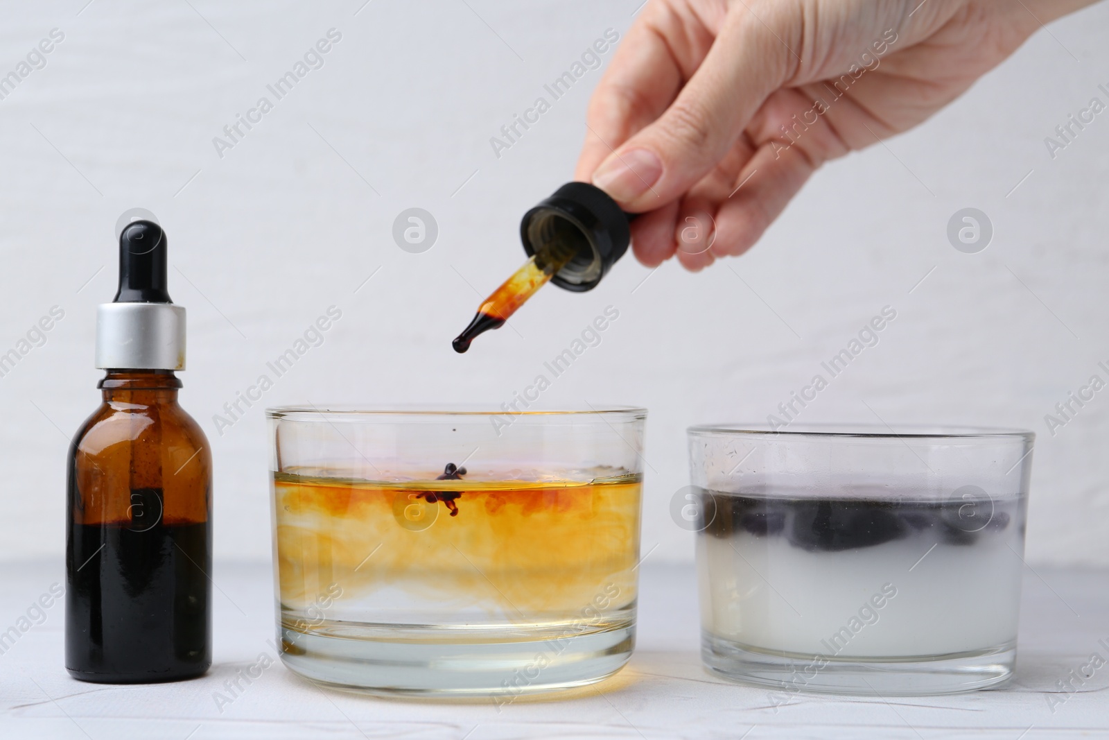 Photo of Iodine starch test. Woman dripping iodine into glass of water at white table, closeup