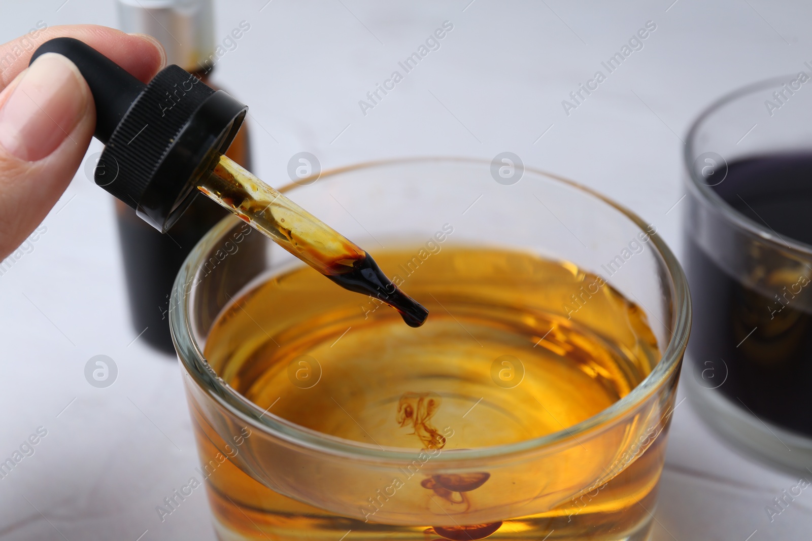 Photo of Iodine starch test. Woman dripping iodine into glass of water at white table, closeup