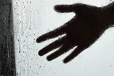 Silhouette of woman behind wet glass, closeup