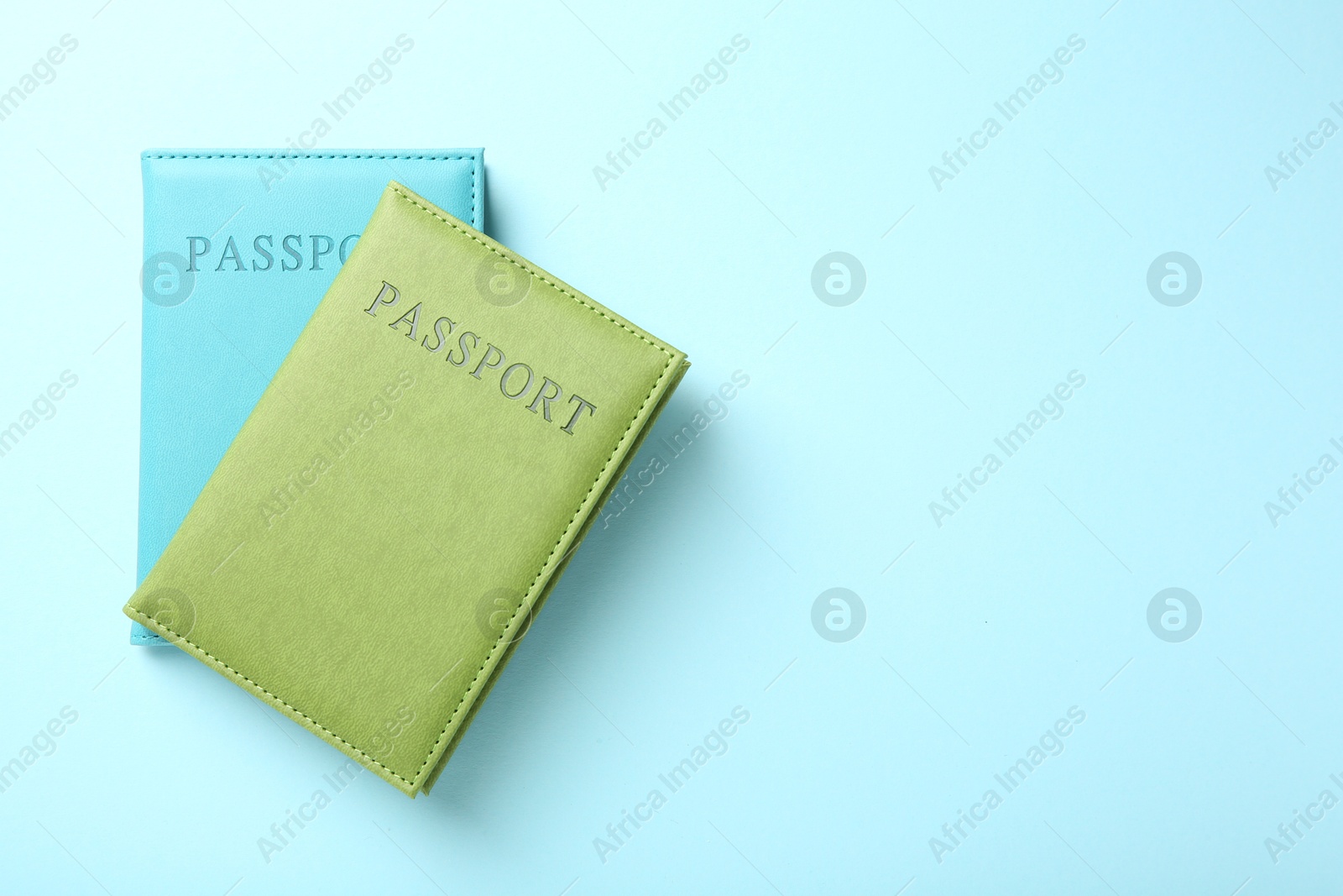 Photo of Passports in color covers on light blue background, top view. Space for text