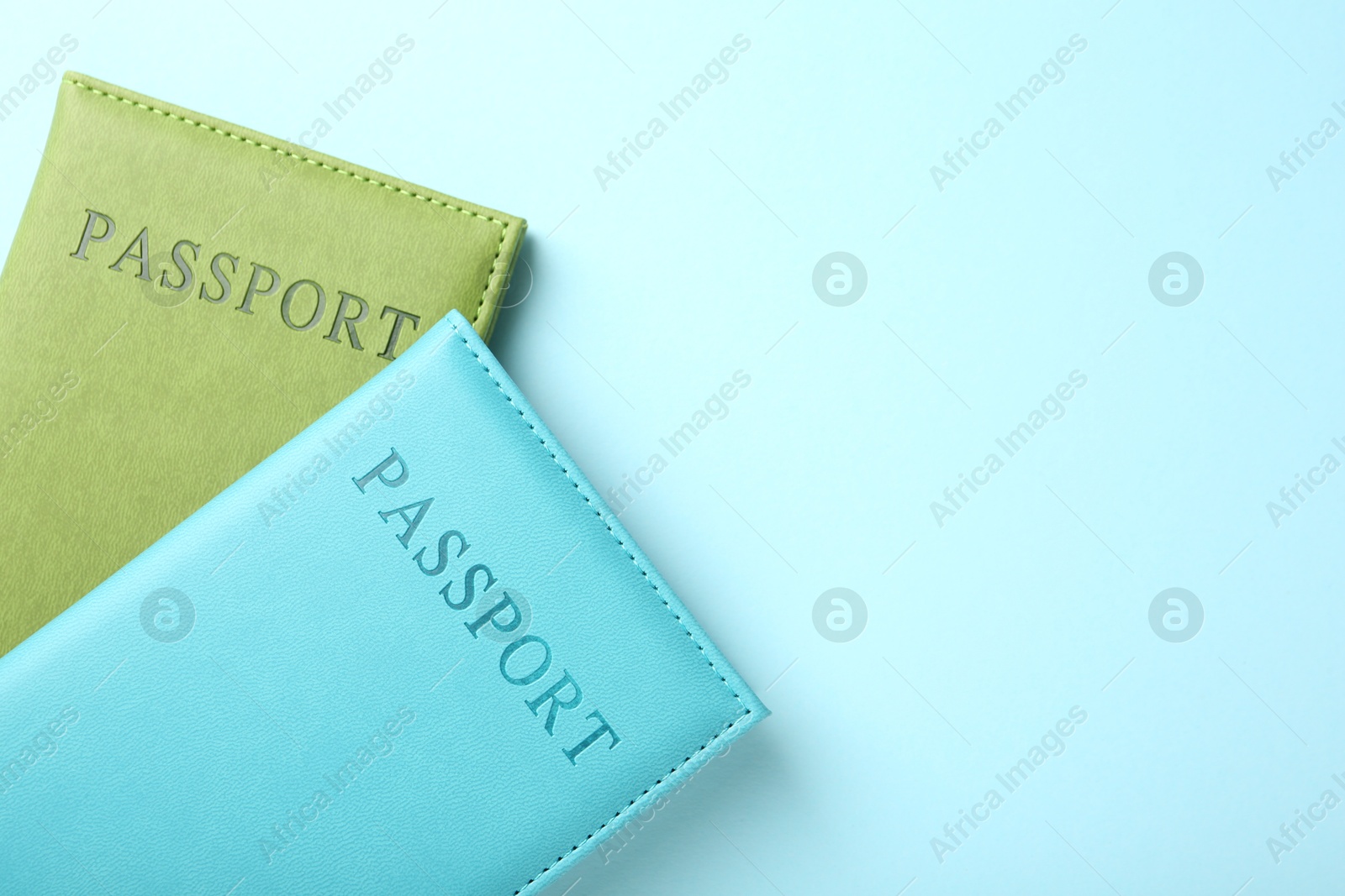 Photo of Passports in color covers on light blue background, top view. Space for text