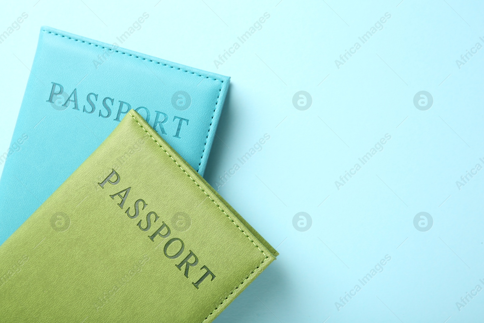 Photo of Passports in color covers on light blue background, top view. Space for text