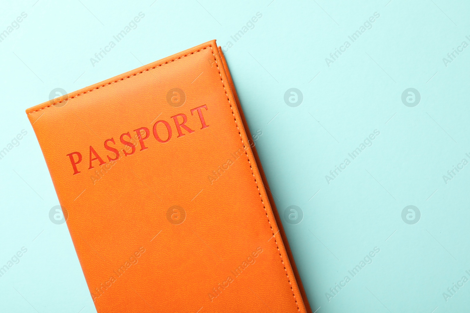 Photo of Passport in orange cover on light blue background, top view. Space for text