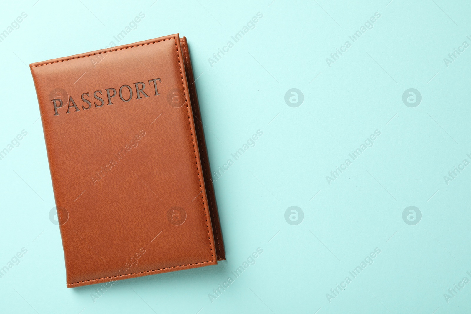 Photo of Passport in brown cover on light blue background, top view. Space for text