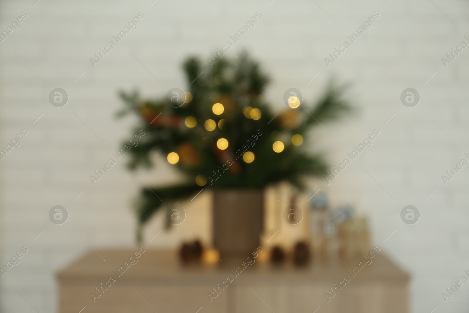 Photo of Blurred view of beautiful Christmas composition with decorated fir tree branches on wooden nightstand near white brick wall