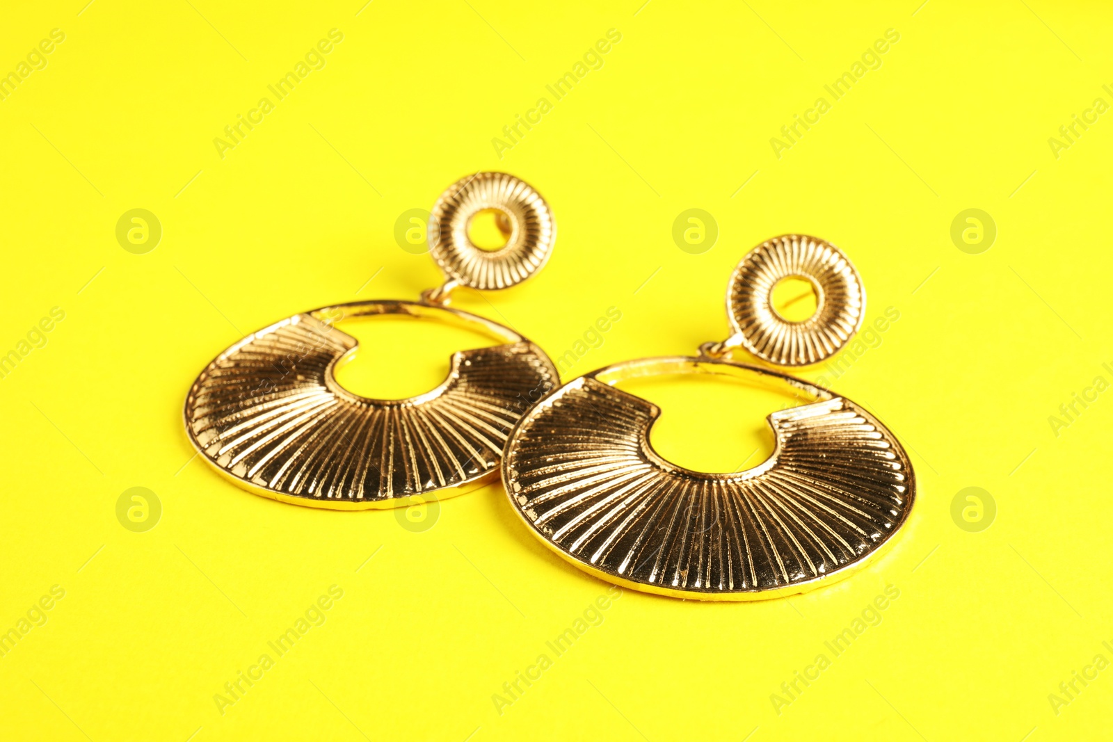 Photo of Beautiful bijouterie. Stylish earrings on yellow background, closeup