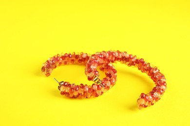 Photo of Beautiful bijouterie. Stylish earrings on yellow background, closeup