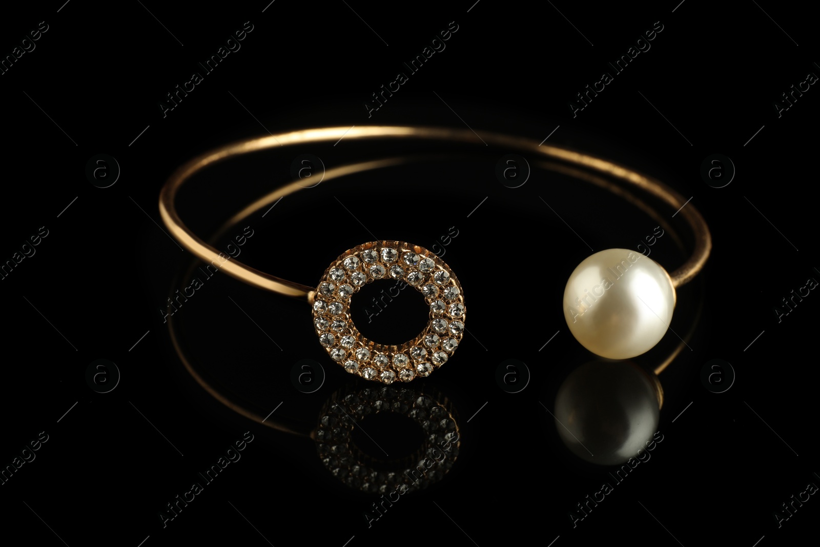 Photo of Beautiful bijouterie. Elegant ring on black mirror surface, closeup