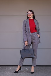 Photo of Beautiful woman in stylish suit near grey wall outdoors