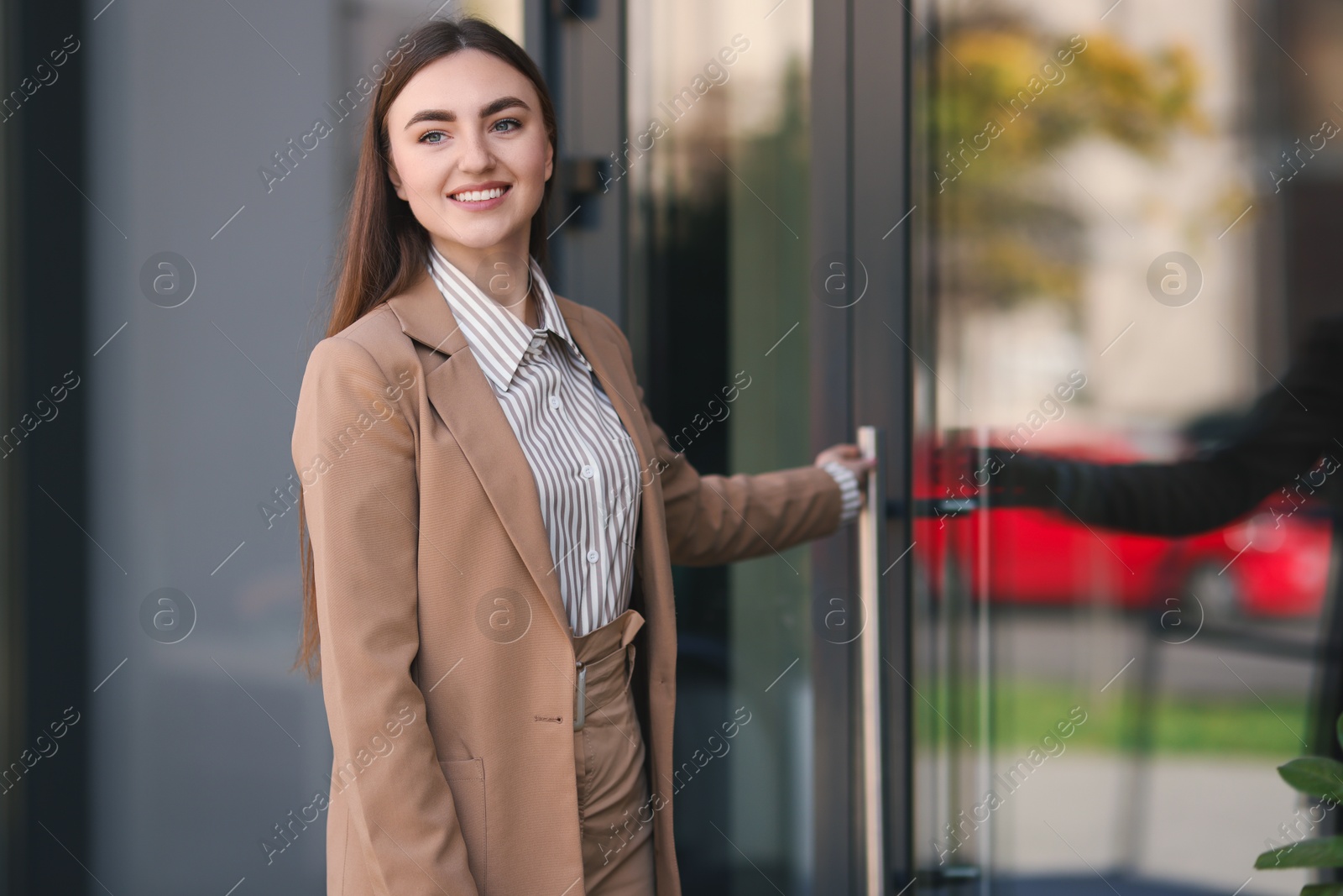 Photo of Smiling woman in stylish suit opening door of business center outdoors