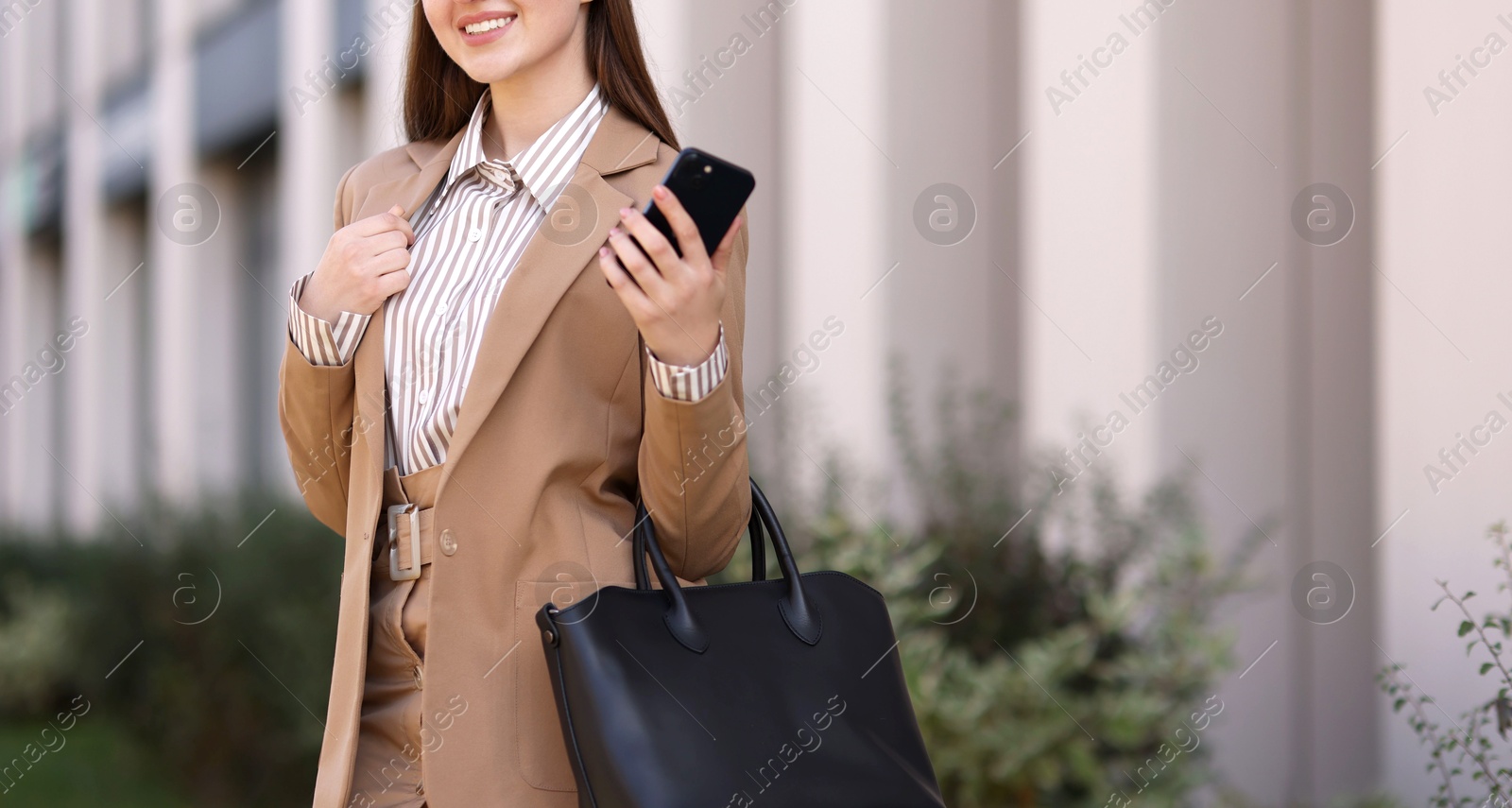 Photo of Smiling businesswoman in stylish suit with smartphone outdoors, closeup. Space for text