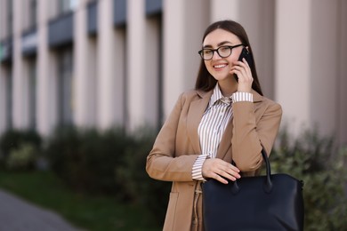 Photo of Beautiful woman in stylish suit talking on smartphone outdoors. Space for text