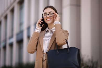 Photo of Smiling businesswoman in stylish suit talking on smartphone outdoors