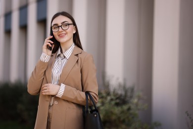 Photo of Beautiful woman in stylish suit talking on smartphone outdoors. Space for text