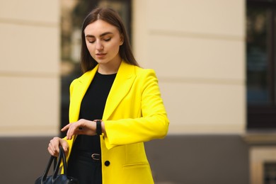 Photo of Businesswoman in stylish suit looking at wristwatch outdoors. Space for text