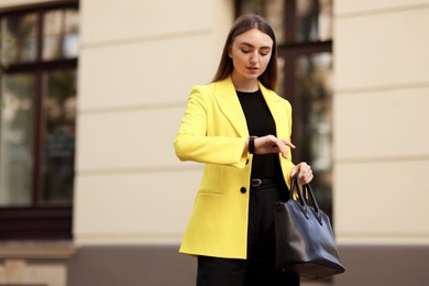 Photo of Businesswoman in stylish suit looking at wristwatch outdoors. Space for text