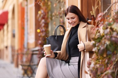 Photo of Smiling businesswoman in stylish suit with paper cup in outdoor cafe. Space for text