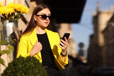 Businesswoman in stylish suit with smartphone outdoors on sunny day