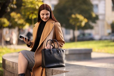 Smiling businesswoman in stylish suit with smartphone outdoors. Space for text