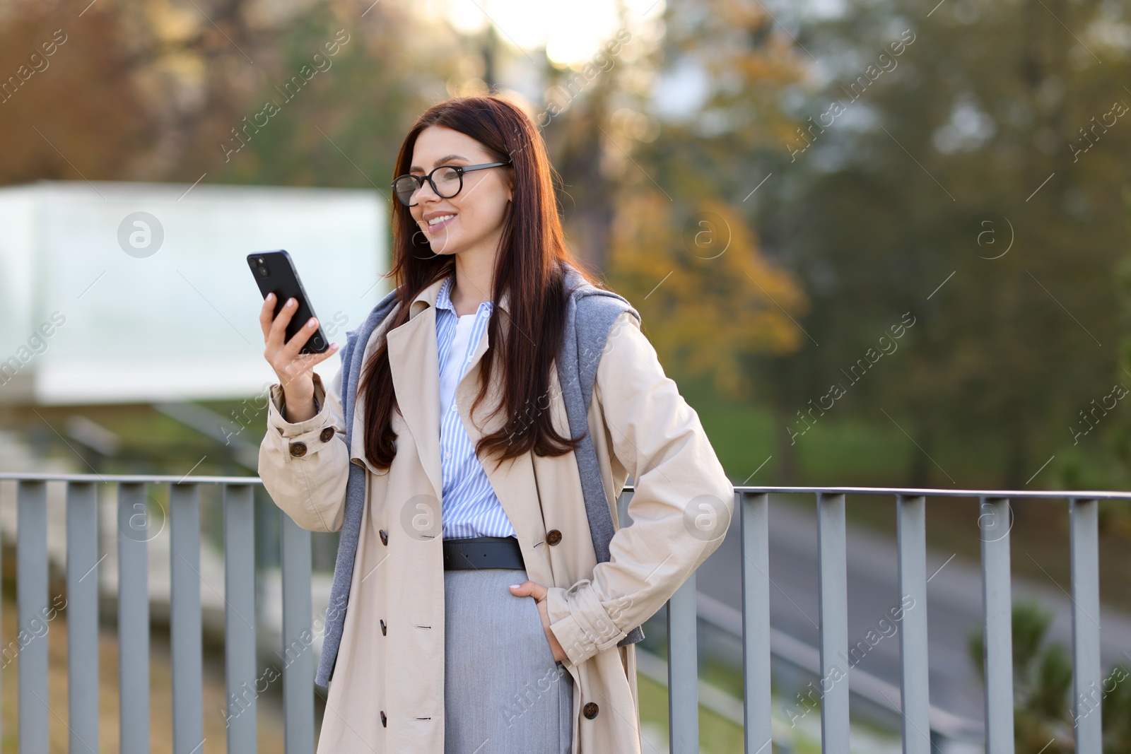 Photo of Smiling businesswoman in stylish suit with smartphone outdoors