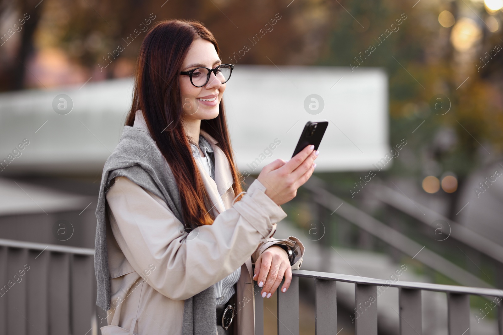 Photo of Smiling businesswoman in stylish suit with smartphone outdoors