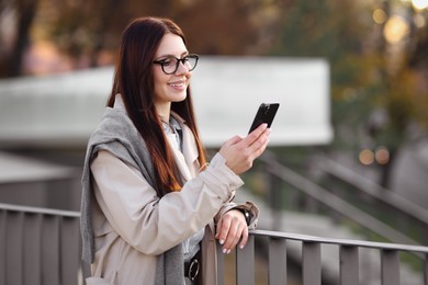 Smiling businesswoman in stylish suit with smartphone outdoors