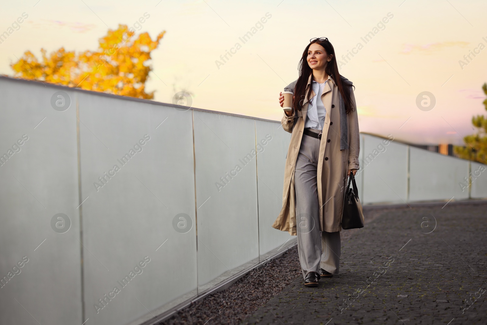 Photo of Smiling businesswoman in stylish suit with paper cup walking outdoors. Space for text