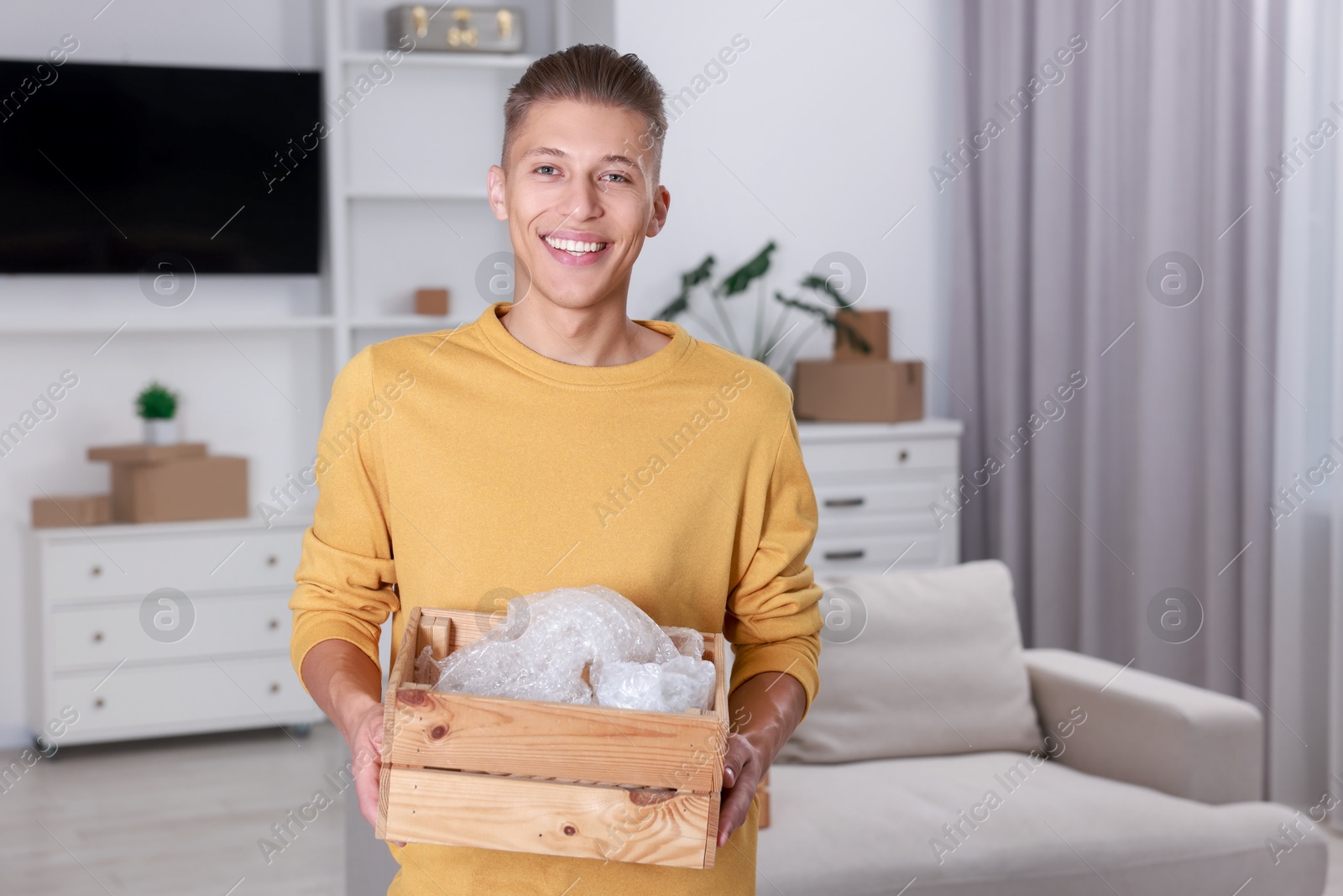 Photo of Happy man holding wooden crate with stuff in new apartment. Housewarming party