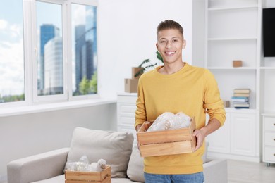 Photo of Happy man holding wooden crate with stuff in new apartment. Housewarming party