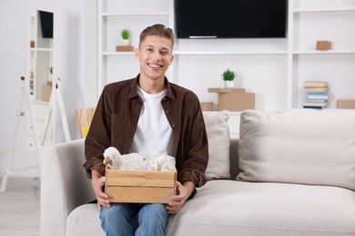 Photo of Happy man holding wooden crate with stuff on sofa in new apartment. Housewarming party