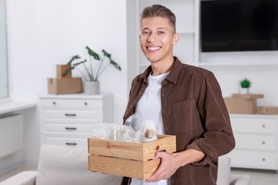 Photo of Happy man holding wooden crate with stuff in new apartment. Housewarming party