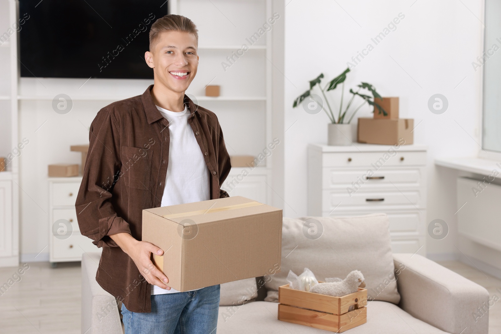 Photo of Happy man with moving box in new apartment. Housewarming party