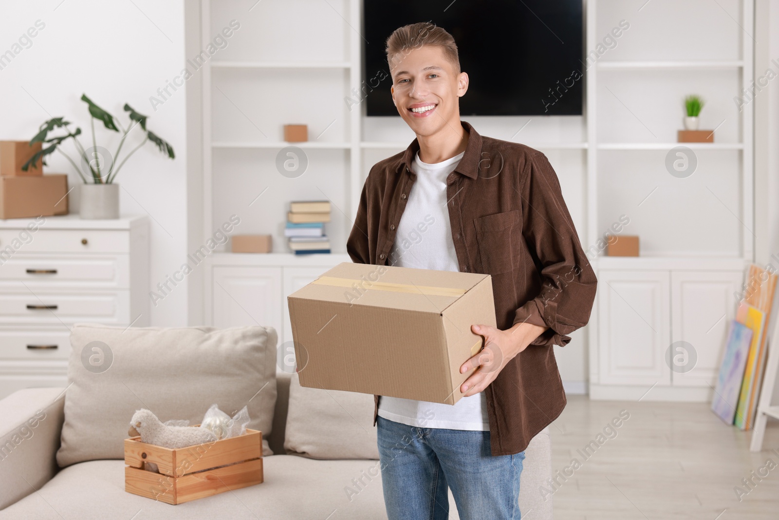 Photo of Happy man with moving box in new apartment. Housewarming party