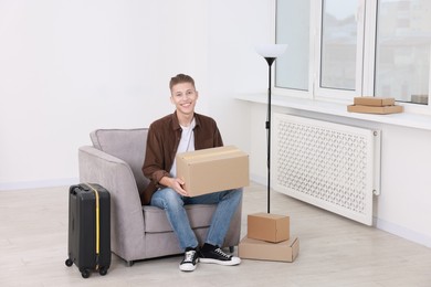 Photo of Happy man with moving boxes and suitcase in new apartment. Housewarming party