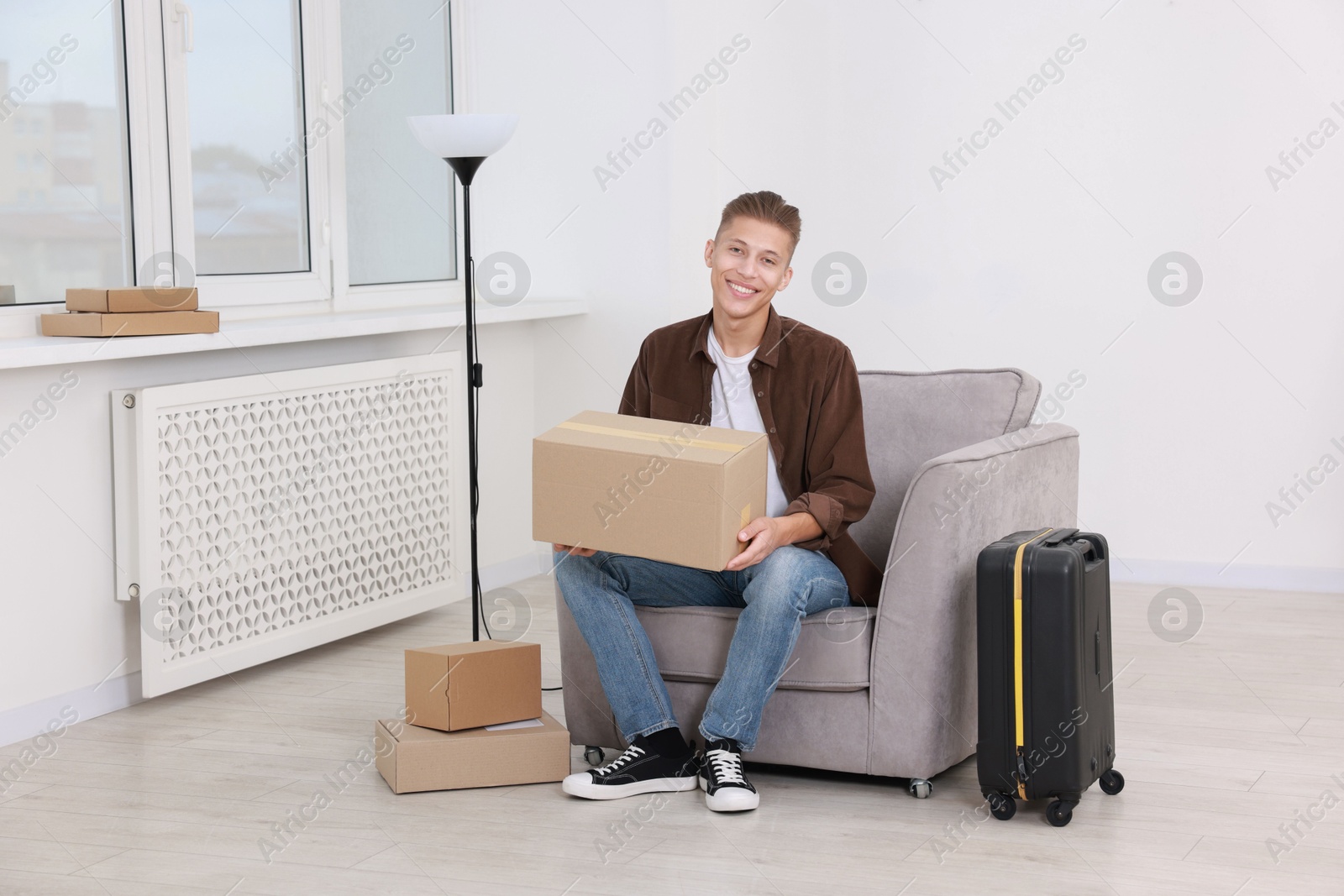 Photo of Happy man with moving boxes and suitcase in new apartment. Housewarming party