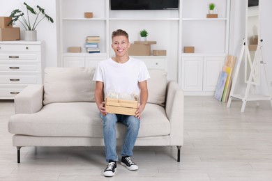 Photo of Happy man holding wooden crate with stuff on sofa in new apartment. Housewarming party