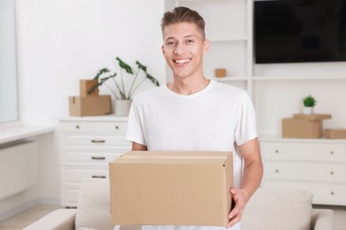 Photo of Happy man with moving box in new apartment. Housewarming party