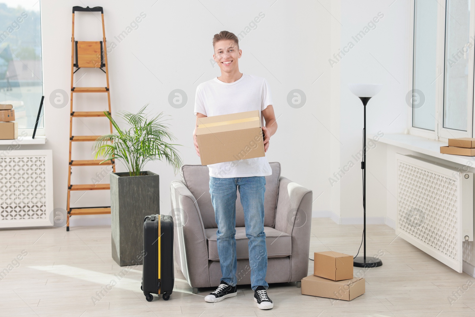 Photo of Happy man with moving boxes and suitcase in new apartment. Housewarming party