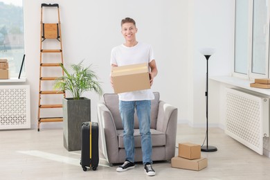 Photo of Happy man with moving boxes and suitcase in new apartment. Housewarming party