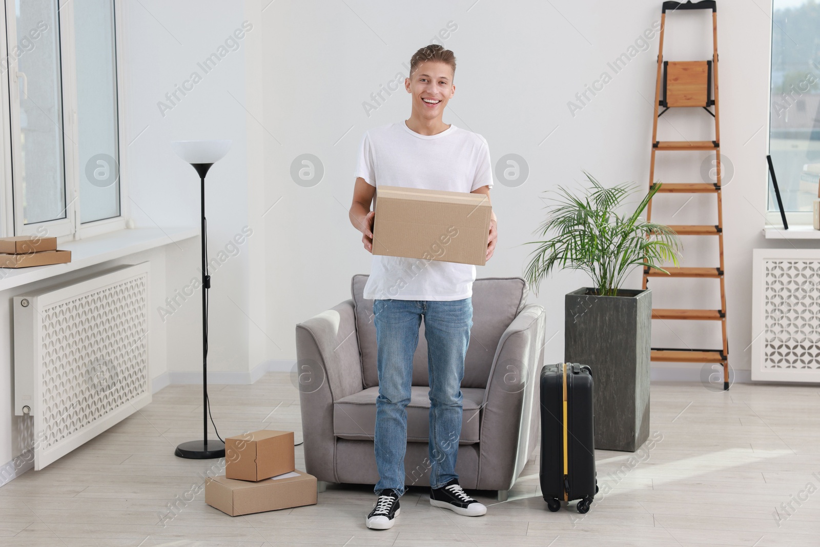 Photo of Happy man with moving boxes and suitcase in new apartment. Housewarming party