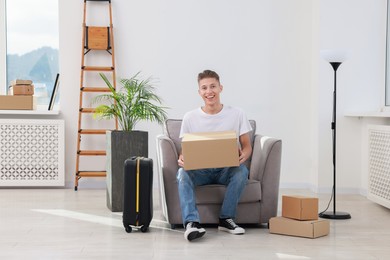 Photo of Happy man with moving boxes and suitcase in new apartment. Housewarming party