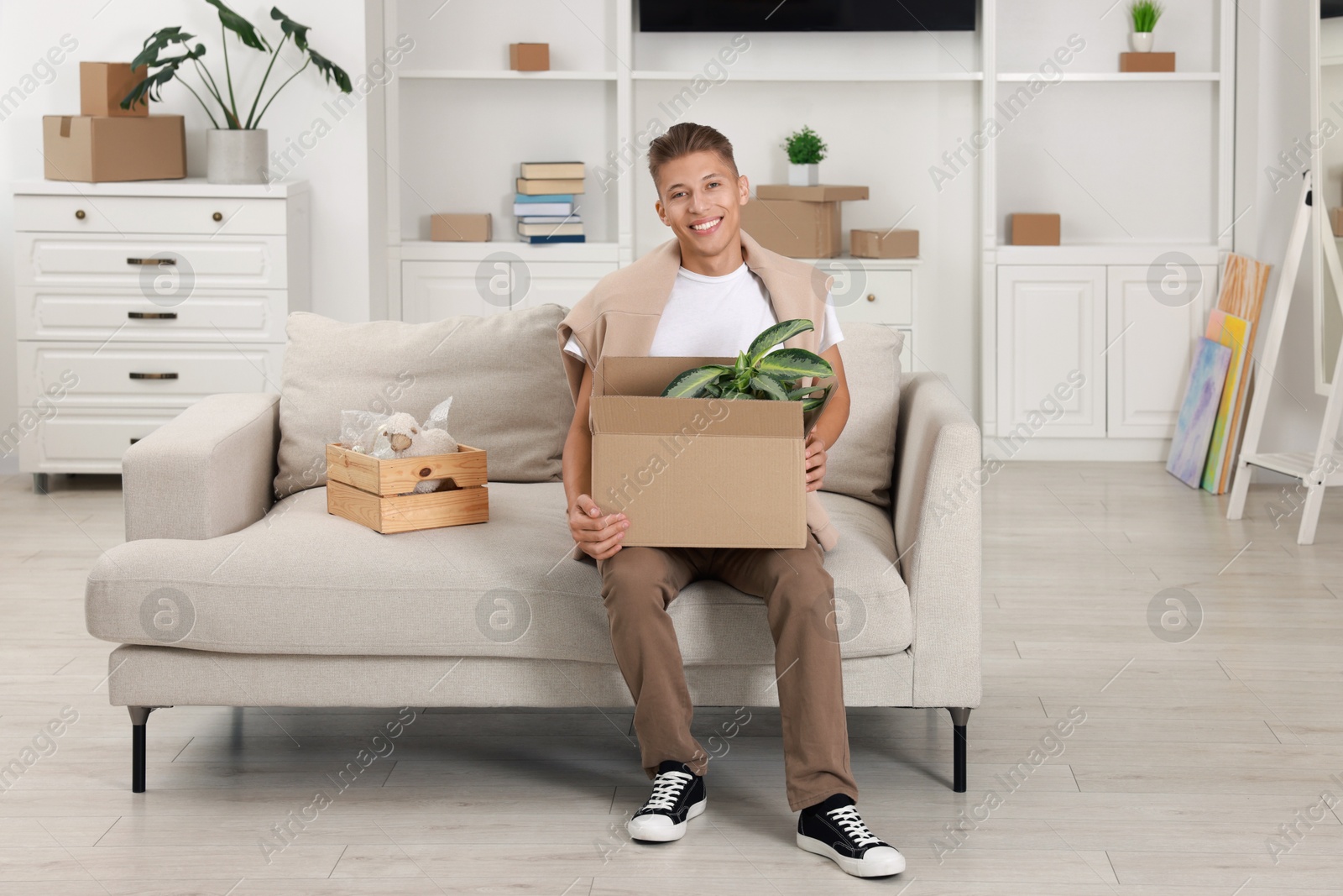 Photo of Happy man holding moving box with houseplant in new apartment. Housewarming party