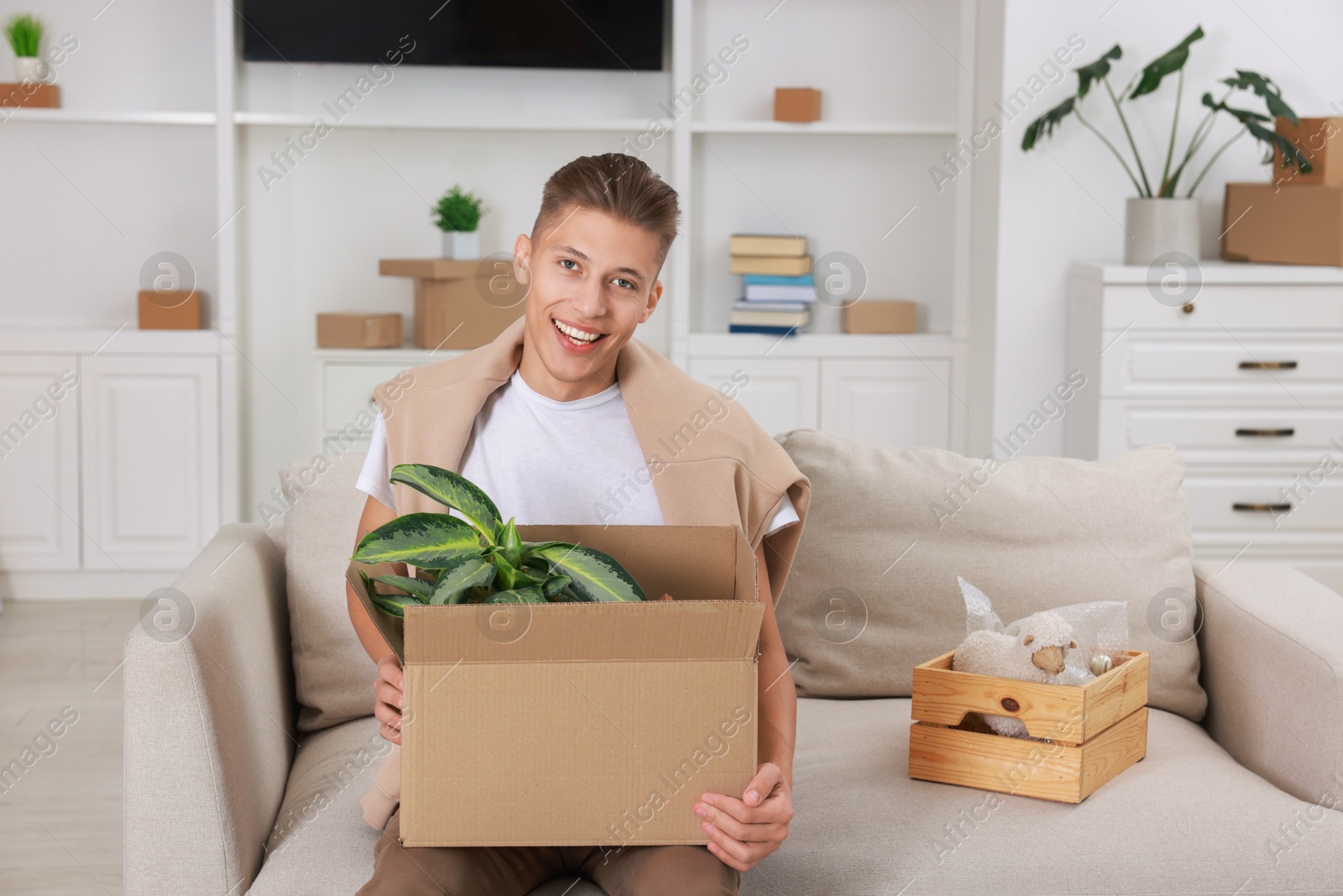 Photo of Happy man holding moving box with houseplant in new apartment. Housewarming party