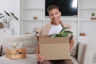 Photo of Happy man holding moving box with houseplant in new apartment. Housewarming party